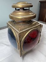 Front left side view of the square brass carriage lantern showing red and blue convex glass lenses on two adjacent sides and vented brass top.
