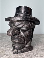Front view of cast iron tobacco container shaped as Mr. Punch with prominent facial features and top hat lid.