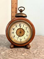 Front view of the large wooden alarm clock showing round wooden case, glass covered dial with large decorative black Arabic numerals and a brass central disc.