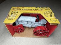 Front view of the Ertl antique Fordson tractor model showing gray body and red metal wheels inside original yellow box with illustrations and text.