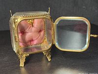 Front and open door view showing detailed interior pink tufted fabric cushion and gilt ormolu frame with beveled glass sides and bottom.