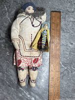 Mother and child Inuit dolls with ruler for scale showing approximate sizes of 7 and 3 inches respectively.
