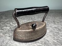 Side view of the miniature sad iron showing black handle and metal body.