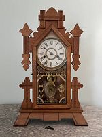 Front view of oak mantel clock, gingerbread style case with decorative cutouts, reverse-painted glass and key laid in front
