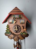 Front view of the wooden cuckoo clock hanging on the wall showing the clock face, colorful bird, deer, tree, and girl on swing below.