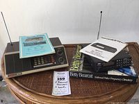 Both scanners placed on a wicker table with manuals and Betty Bearcat National Police Frequency Directory book.