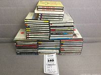 Stacked pile of about 45 classical and instrumental music CDs in jewel cases, arranged in multiple stacks on a cushioned surface with neutral background. CDs appear in mostly good physical condition.