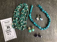 Full view of two turquoise and mother-of-pearl necklaces and three pairs of earrings on gray background