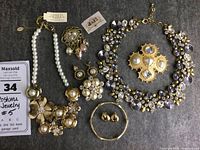 Full view of all jewelry pieces including two necklaces, two brooches, two pairs of earrings, and one bangle on dark fabric background.