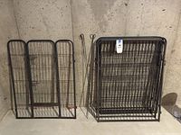 7 metal panels including one with gate door, stack of additional panels and metal ground spikes, all displayed against concrete wall.
