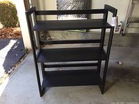 Front view of the black wood folding bookcase showing four shelves, black finish, and folding frame design.