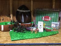 Photo showing the assortment of football-themed party items including three football bowls, mini football candles, black garland, and green turf-like tablecloth.