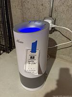 Full view of white cylindrical Hunter air filter unit plugged in, with blue LED lit on top and perforated air intake bottom section visible.