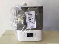 Full view of humidifier wrapped in plastic showing white base and transparent gray water tank.