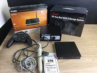 Full image of six electronic devices on wooden table showing a router box, storage system box, game controller, joystick switch, microphone and slim DVD drive