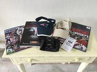 Overview of sports memorabilia and accessories on a cream-colored table including two Patriots programs, a Red Sox book, two hats, and binoculars.