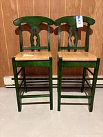 Front view of two wooden bar stools with natural seats and green painted backs and legs.