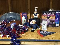 Photo of Patriots collectibles showing covered snack tray, footballs, garland, player figures, books, commemorative glass, and pennants on plywood surface.