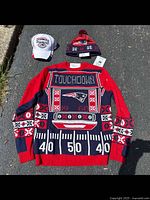 Front view of a red, navy, and white Patriots sweater laid flat with matching knit and baseball hats.