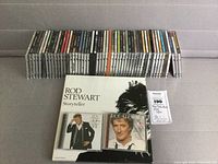 Wide view of entire CD collection lined up in clear jewel cases on a gray surface with Rod Stewart anthology box set front and center.