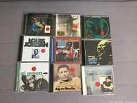 Front view of 7 CDs showing artists including Corey Harris, John Lee Hooker, Jots Jordan, Al Green and Aaron Neville with red sticker marks on covers.
