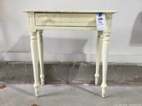 Front view of the shabby painted side table showing the single drawer and four turned legs, with some paint wear visible.