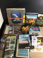 Photo shows a group of simulation manuals including Train Simulator, Combat Commander, Falcon 4 keyboard cover, F-22, SU-27, 777-200 user manual, and World Encyclopedia of Civil Aircraft.