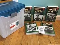 Five WWII military history books and a plastic storage box arranged on wood floor against a green wall. Shows full set and the storage container included.