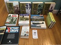 Photo showing multiple WWII books arranged on the floor, titles include Cross Channel Attack, The Last Offensive, Okinawa, Guadalcanal, The Road to Berlin, All American All the Way, Aircraft of WWII, Victory in Europe, and For Our Fathers.