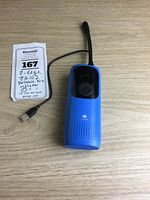 Front view of the blue portable tire inflator with digital display and attached USB cable, placed on a wooden surface with a handwritten lot tag.