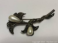 Front view of the brooch showing two faux pearl flowers and marcasite-set silver leaves and stem.