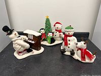 Full view of the five plush snowman and penguin holiday figures on a black surface.