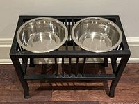 Front angled view of the large black metal elevated dog bowl holder with two shiny stainless steel bowls inserted, showing overall design and color.