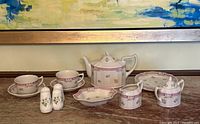 Full display of the Laura Ashley white and pink china tea set showing teapot, cups, saucers, plates, cream jug, sugar bowl, divided serving dish, and salt & pepper shakers on table.