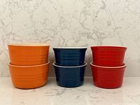 Front view showing two stacked, larger orange ramekins on left, two stacked smaller blue ramekins in middle, two stacked smaller red ramekins on right.