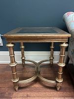 Front view of gold end table showing square glass top, turned bamboo style legs and curved X-shaped stretcher.