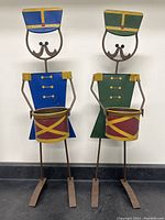 Full front view of two metal nutcracker drummer stands side by side showing height and structure