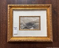 Front view of watercolor landscape painting with ornate gold frame on a wood surface.