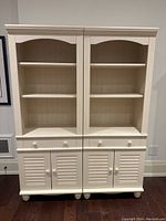 Front view of two identical white wooden bookshelves side by side showing shelves, drawer, and cabinet doors.