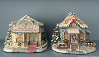 Front view of both Precious Moments Hawthorne Village sculptures, showing Merry Matinee Theater on the left and Jolly Inn Restaurant on the right, both winter themed with snow and holiday decorations.
