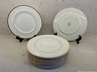 Full view of 13 stacked fine bone china plates, gold and white with gold rims visible, two plates upright showing front and back.