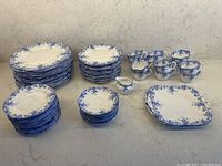 Full set of Shelley Dainty Blue dinnerware arranged on countertop, showing stacks of plates, cups, saucers, creamer, trays, and tiered serving plates