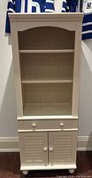 Front view of white bookcase with two shelves, drawer panel and lower cabinet