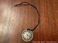 Full view of the David Yurman North Star pendant on a black cord against wooden background.