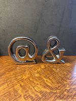 Front view showing silver-colored @ and & figurines on wood surface against dark background