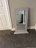 Grey framed rectangular mirror leaning against wall showing frame and reflective glass