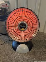 Front view of the Presto HeatDish electric heater lit up showing the glowing heating element behind the protective grill.