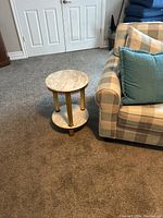 Full view of two-tier round end table next to a couch, showing marble tops and brass legs.