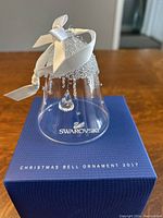 Photo of clear crystal bell ornament with white satin bow on original blue Swarovski box showing logo and text