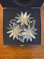 Top view of the Swarovski crystal flower arrangement showing three daisy flowers with detailed petals and textured centers set on a cushion in original box.